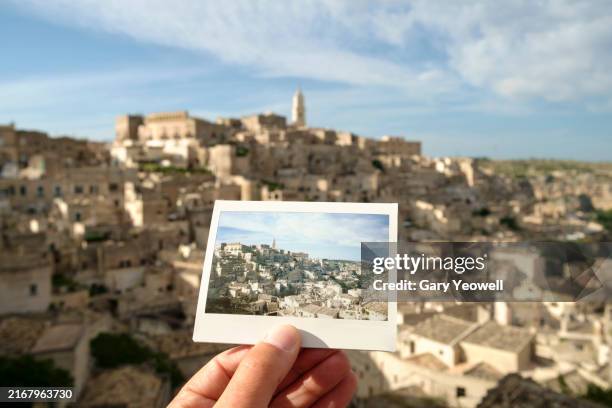 man holding an instant film photo of matera in front of the scene - southern italy stock pictures, royalty-free photos & images