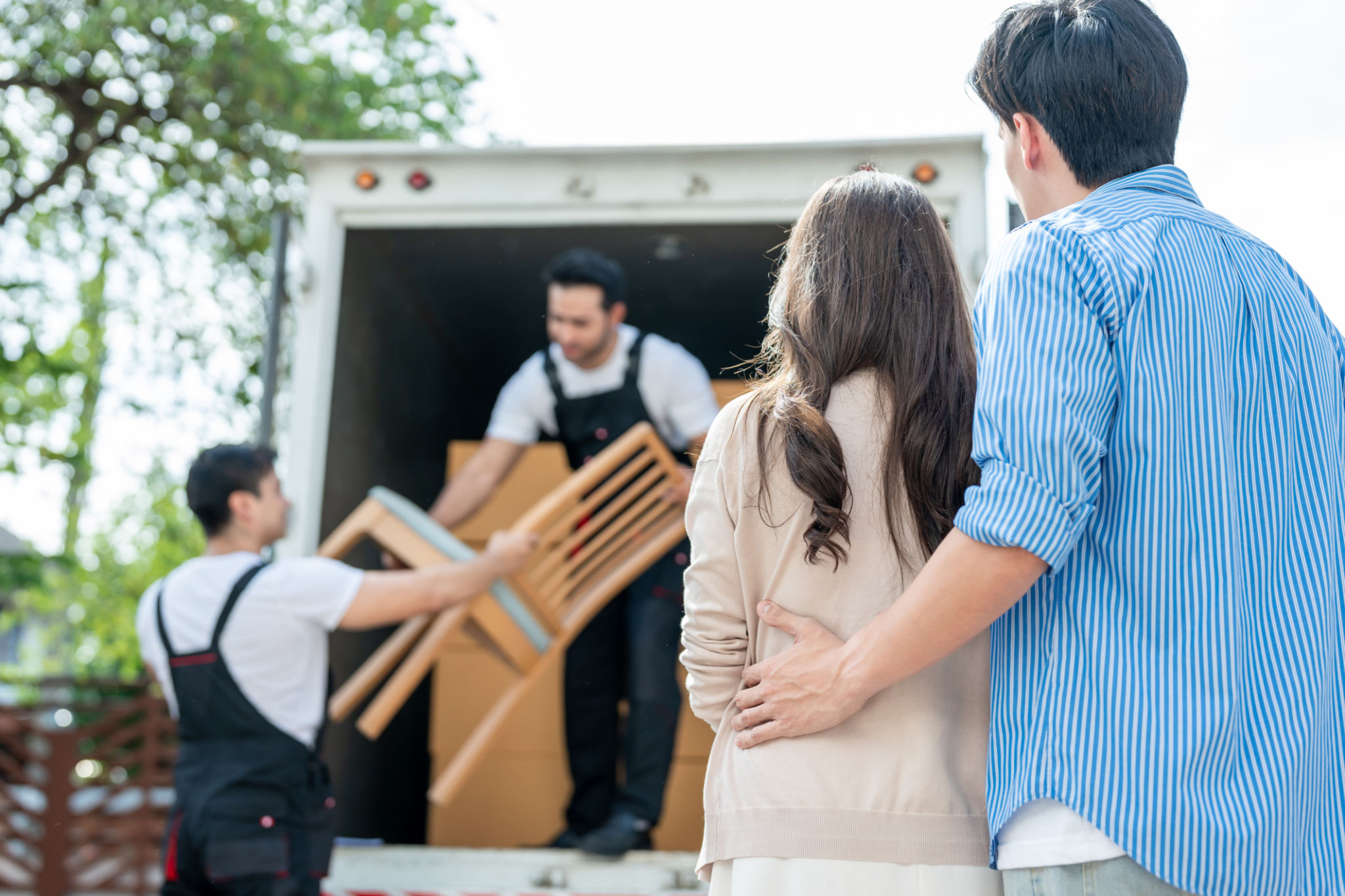Caucasian delivery man worker delivering package to young couple in house. Attractive courier employee working and deliver box cardboard from car truck infront of new house of new marriage partner. Caucasian delivery man worker delivering package to young couple in house. Attractive courier employee working and deliver box cardboard from car truck infront of new house of new marriage partner.