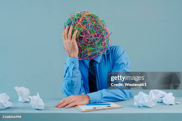 thoughtful businessman with mask of chaotic thoughts against blue background - burnout psychischer zustand stock-fotos und bilder