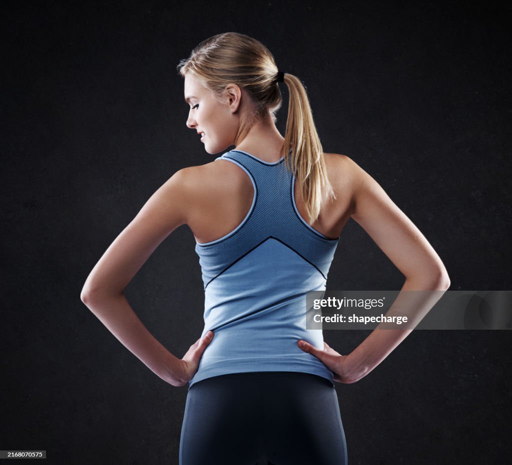 Woman, back and fitness with confidence in studio for health and wellness on a black background. Active female person or young model with hands on hip in fashion for sports, workout gym or training