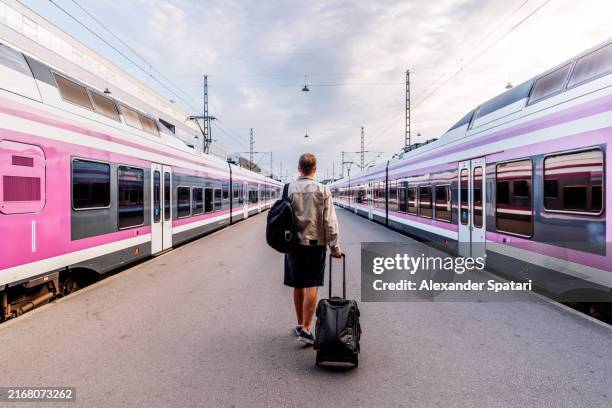 rear view of a man with backpack and suitcase walking among trains on the train station, helsinki, finland - helsinki railway station stock pictures, royalty-free photos & images