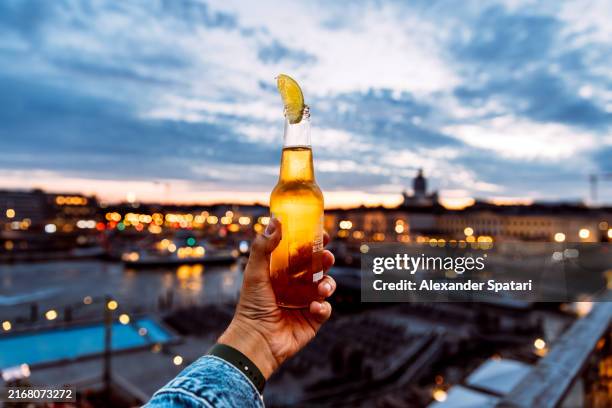 man holding bottle of beer with lime at sunset, personal perspective view - helsinki beer stock pictures, royalty-free photos & images