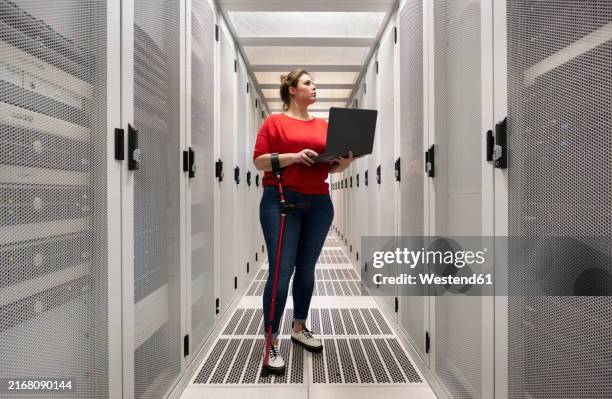 engineer with physical disability holding laptop and working in server room at data center - crutch stock pictures, royalty-free photos & images