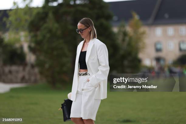Fashion Week guest is seen wearing aviator sunglasses with brown frame and grey lenses, several silver earrings and studs, a silver necklace, a white...