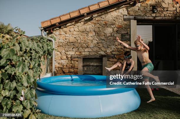 children playing joyfully by a backyard inflatable pool during a sunny afternoon at a rustic home surrounded by nature - teich garten stock-fotos und bilder