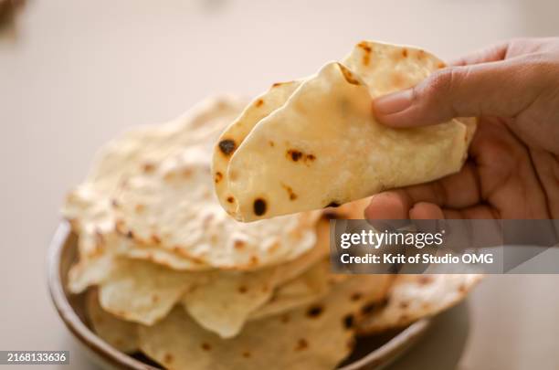 hand picking a freshly made roti from a stack on a plate - naan bread stock pictures, royalty-free photos & images