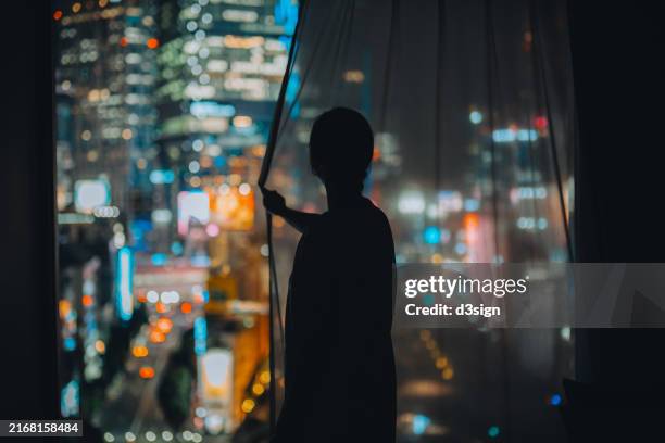 silhouette of young asian woman standing in front of window with illuminated and iconic cityscape of tokyo at night, closing the curtains - shinjuku cocoon building fotografías e imágenes de stock