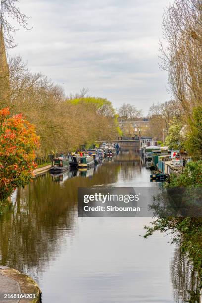 Wooden houseboats and boats docked and moored on Regent's Canal in the residential district of Maida Vale in Little Venice, London, under a cloudy sky.