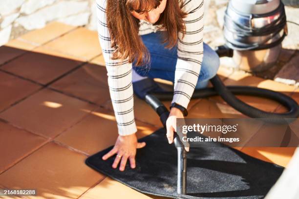 a woman bending down to clean the carpet of her car with a vacuum cleaner illuminated by the sun's rays in the background part of her car can be seen. - car carpet stock pictures, royalty-free photos & images