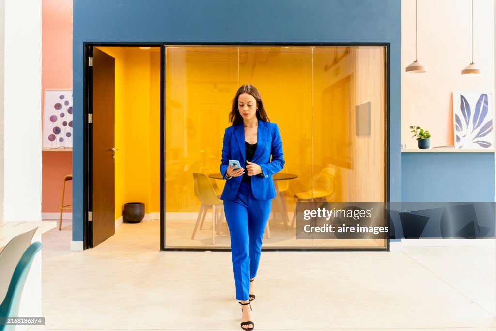 Young smiling long-haired woman elegantly dressed holding a pen in her hand standing looking at the camera inside her office