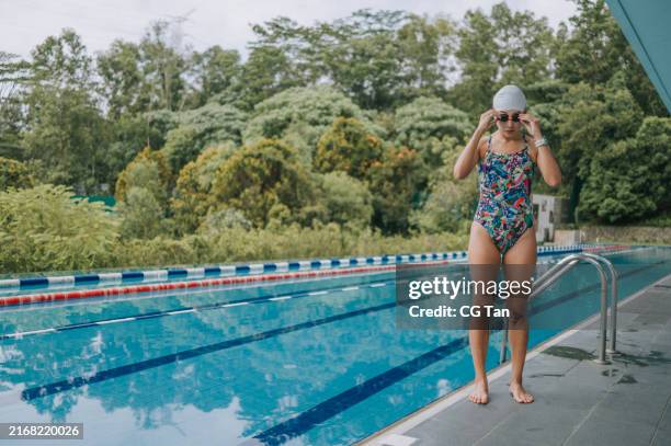 asian chinese female swimmer putting on swimming goggle standing at the edge of swimming pool getting read - swimmer stock pictures, royalty-free photos & images