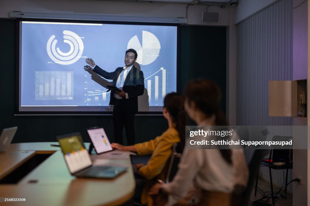 Asian businessman leads a dynamic presentation in a professional meeting room with corporate executives, showcasing business strategy and team collaboration for strategic growth and success.