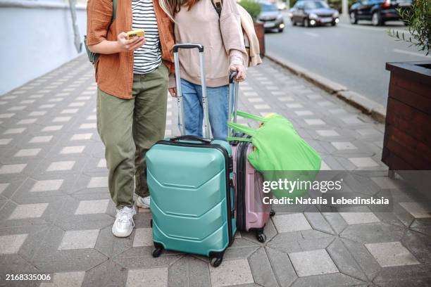 urban adventure: two unrecognisable teenage girls with backpacks and suitcases, waiting for a taxi and navigating the city with a smartphone during their travel. - wheeled luggage stock pictures, royalty-free photos & images