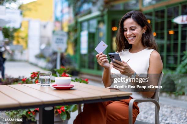 woman in cafe looking at smartphone holding a card - e commerce stock pictures, royalty-free photos & images