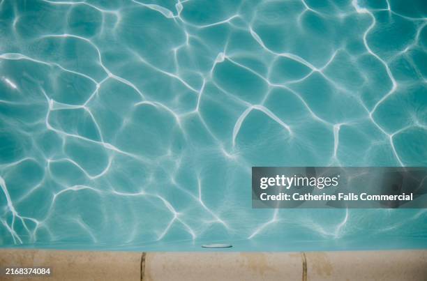 calm turquoise water with sunlit reflections in a swimming pool surrounded by a light-colored paving surface on a clear day - travel essentials stock pictures, royalty-free photos & images