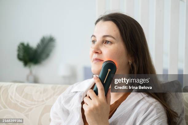 una donna caucasica si massaggia il viso con un massaggiatore elettrico. - massaggio del viso foto e immagini stock