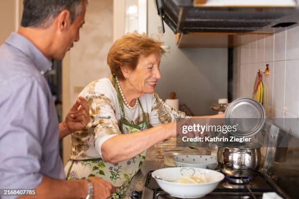 elderly woman and her nephew in the kitchen, cooking together - italiaanse etniciteit stockfoto's en -beelden