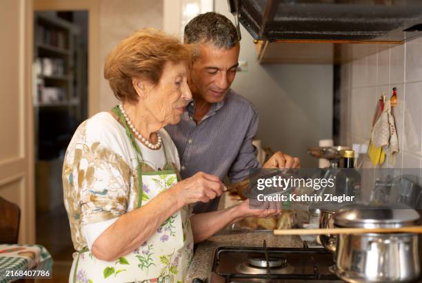 elderly woman and her nephew in the kitchen, cooking together - italiaanse etniciteit stockfoto's en -beelden