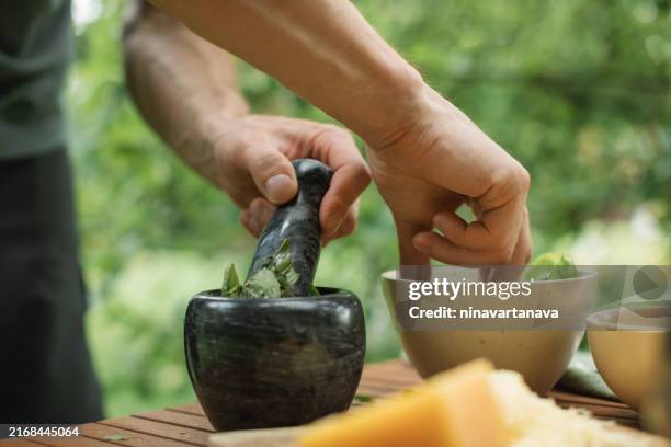 close-up of a man making fresh basil pesto sauce with pine nuts, parmesan and basil - mortaio con pestello foto e immagini stock