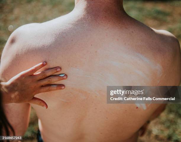 a child applying sunscreen on an adult's back during a sunny day outdoors at the park, ensuring protection from harmful uv rays - irritation cutanée photos et images de collection