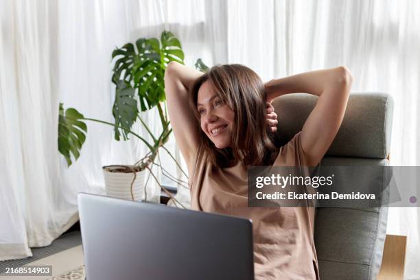 woman sitting in a chair in front of a laptop, cheerful atmosphere, wearing a muscle t-shirt, woman with brown hair - hands behind head stock pictures, royalty-free photos & images