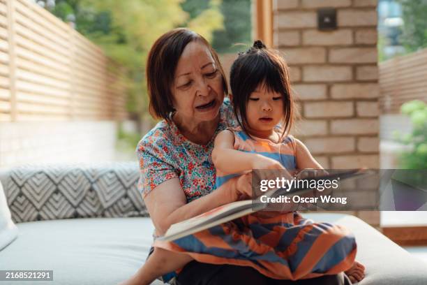 asian grandmother reading to her granddaughter - east asian people stock pictures, royalty-free photos & images