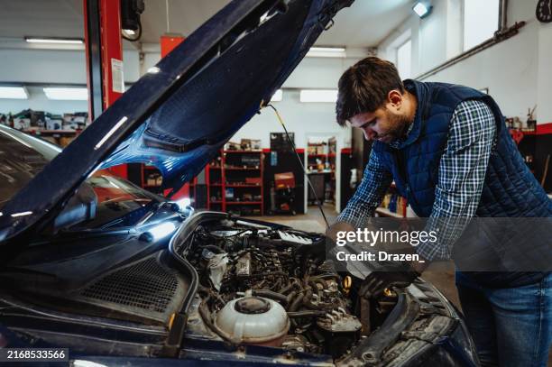 mecánico de automóviles que arregla el automóvil en un taller de reparación de automóviles. joven ingeniero revisando el coche y arreglando piezas electrónicas - mecánico fotografías e imágenes de stock