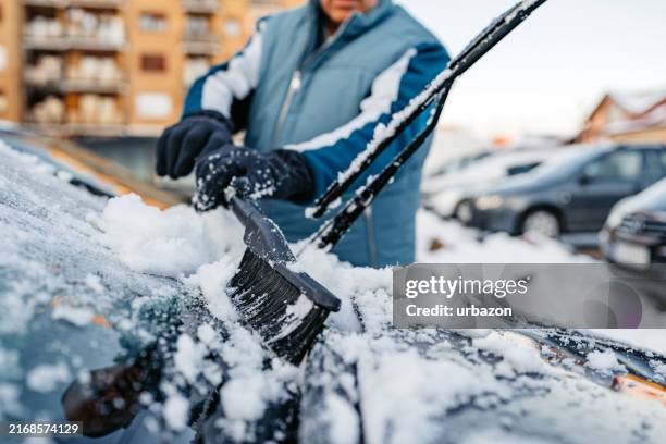 senior man cleaning snow off his car on the parking lot - quitahielo fotografías e imágenes de stock