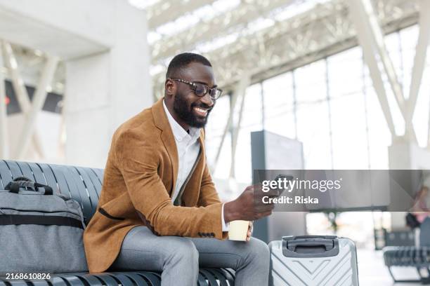 hombre de negocios sonriente usando teléfono inteligente en la sala de salidas de la estación - viaje de negocios fotografías e imágenes de stock