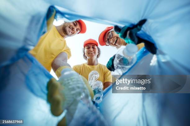 pov shot from blue garbage bag, volunteers throwing plastic bottles while looking at camera - recycling stock pictures, royalty-free photos & images