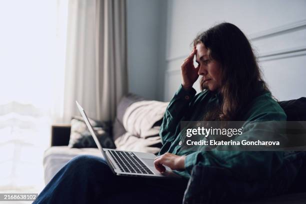 woman working on laptop at home. she looks stressed while sitting on a sofa in a bright room. copy space on the left side. - grief at work stock pictures, royalty-free photos & images
