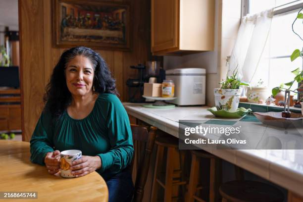 hispanic woman sitting in her kitchen - zwart haar stockfoto's en -beelden