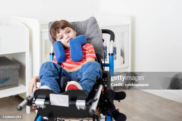 menino bonito com paralisia cerebral em sua cadeira de rodas que olha a câmera - cadeira de rodas equipamento ortopédico - fotografias e filmes do acervo