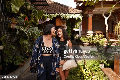 Mother and daughter laughing while walking in street market on sunny day Mother and daughter laughing while walking in street market on sunny day