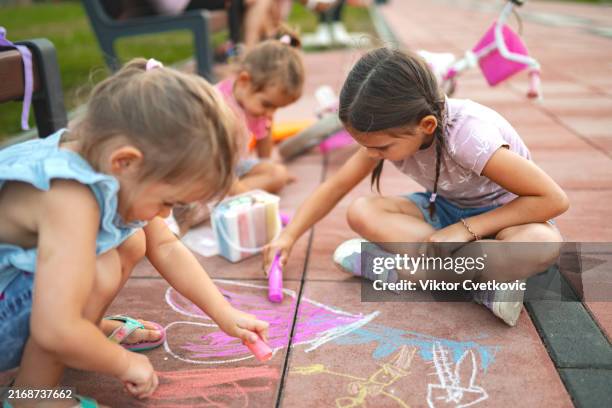 bambini che si divertono a giocare all'aperto mentre creano colorati gessetti artistici in una giornata di sole nel parco con scooter nelle vicinanze - gessetto da lavagna foto e immagini stock