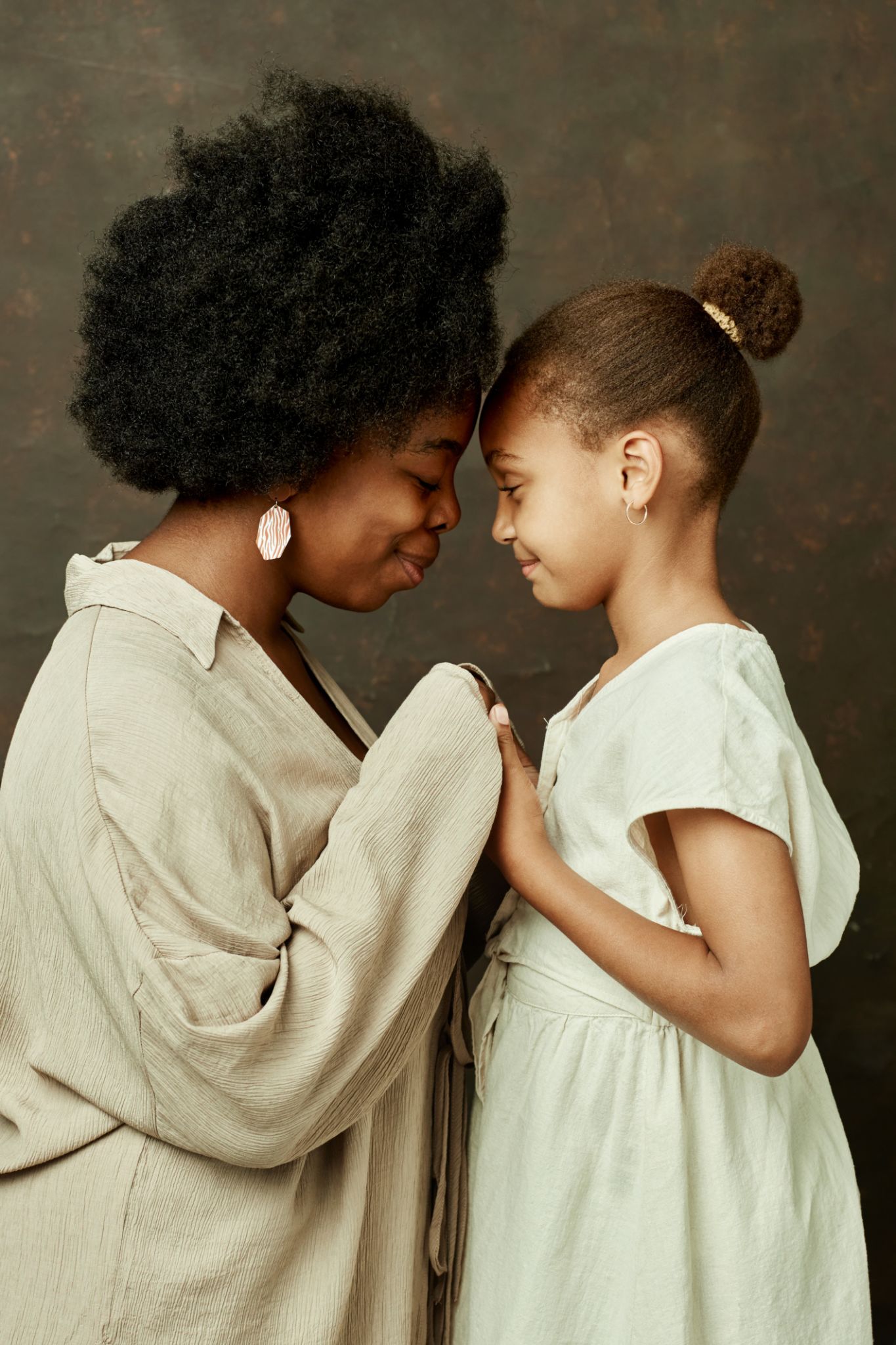 Curly Black Mother and Daughter Holding Hands Smiling on Brown Background Curly Black Mother and Daughter Holding Hands Smiling on Brown Background
