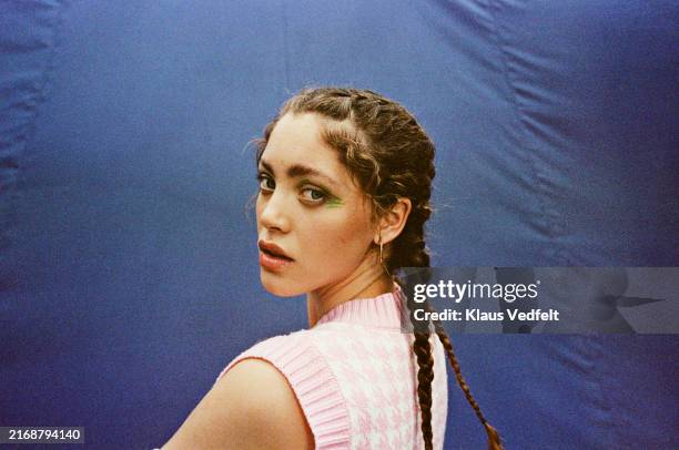 portrait of young woman with braids looking over shoulder against blue backdrop - regarder par dessus son épaule photos et images de collection