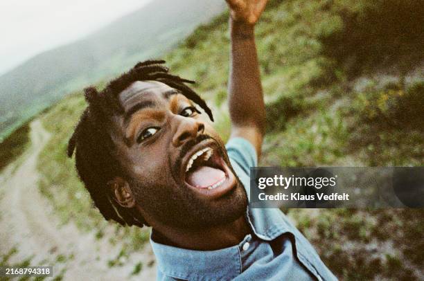 portrait of young man screaming in field at safari resort - selfie stockfoto's en -beelden