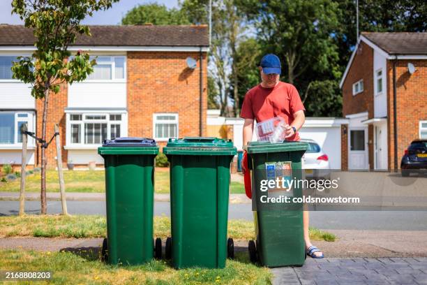 mid adult man putting plastic waste in recycling bin on residential street - balde de lixo imagens e fotografias de stock