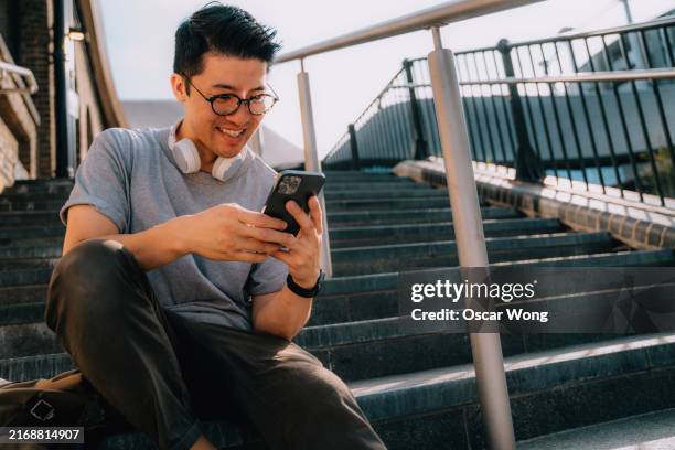 young asian man sitting on city staircase using smartphone - mobile game stock pictures, royalty-free photos & images