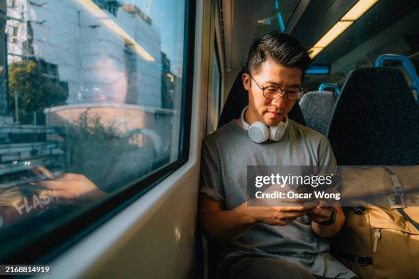 young asian man sitting on train using smartphone - rush hour stock pictures, royalty-free photos & images