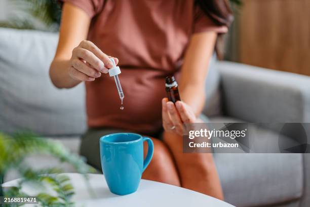 donna asiatica incinta di metà adulto che mette gocce di medicina in un bicchiere d'acqua - omeopatia foto e immagini stock