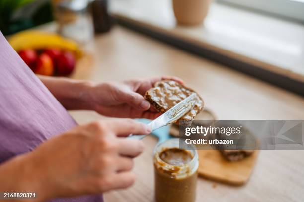 mid-adult pregnant asian woman preparing a peanut butter sandwich in the kitchen at home - peanut butter stock pictures, royalty-free photos & images