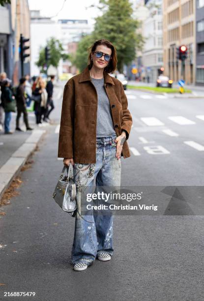 Marianne Theodorsen wears brown wild leather jacket, denim jeans with print, blue bag, grey short at Oslo Fashion Week 2024 on August 27, 2024 in...