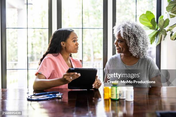 in home healthcare provider consulting with senior female in her home - medicare fotografías e imágenes de stock