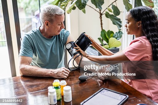 In home healthcare provider measuring senior man's blood pressure in his home In home healthcare provider measuring senior man's blood pressure in his home