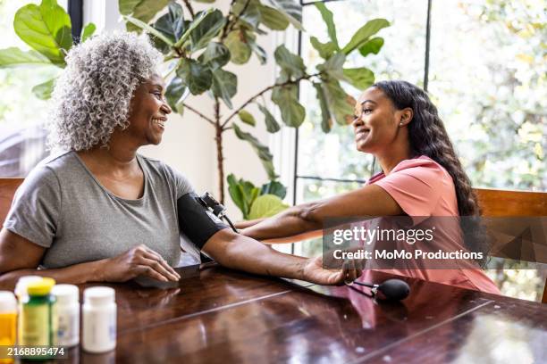 in home healthcare provider measuring senior woman's blood pressure in her home - bluthochdruck stock-fotos und bilder
