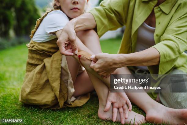 mother treating her daughter's injury. injured, bleeding elbow after fall. mom holding band aid and soothing crying girl. - elbow stock pictures, royalty-free photos & images