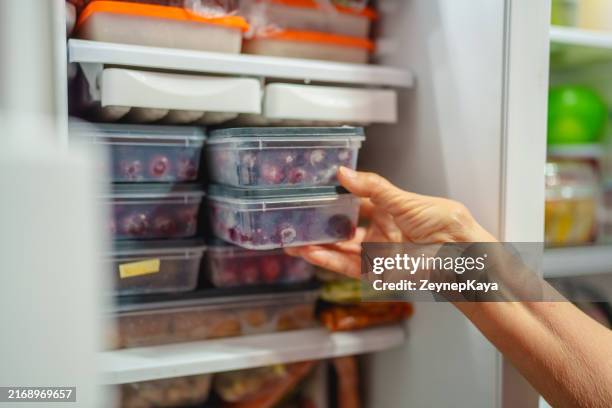 an elderly woman is arranging storage containers in her freezer. - comida congelada comida imagens e fotografias de stock