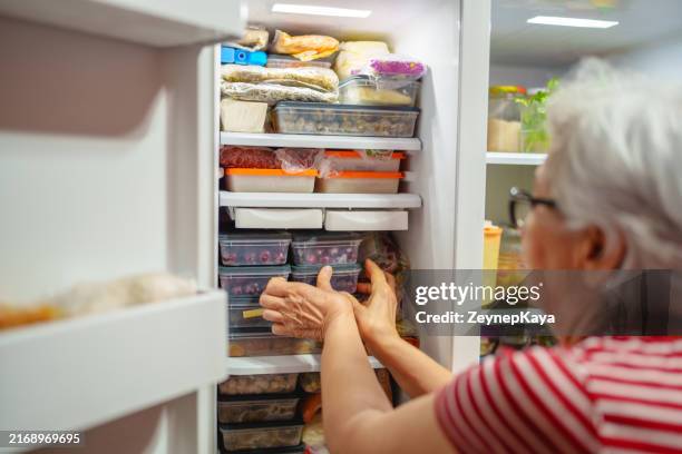 an elderly woman is arranging storage containers in her freezer. - frys bildbanksfoton och bilder